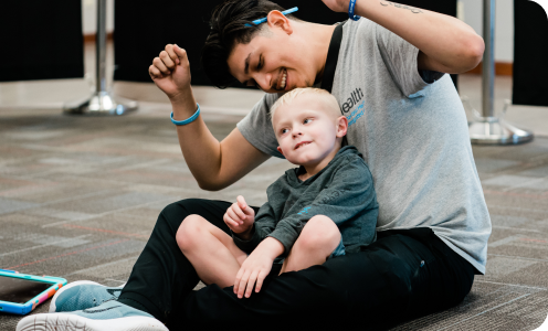 A young adult and a child sitting together on a carpeted floor, smiling.