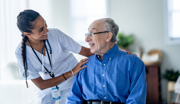 Image of a medical professional talking to and smiling with an elderly man with her hands on his shoulders