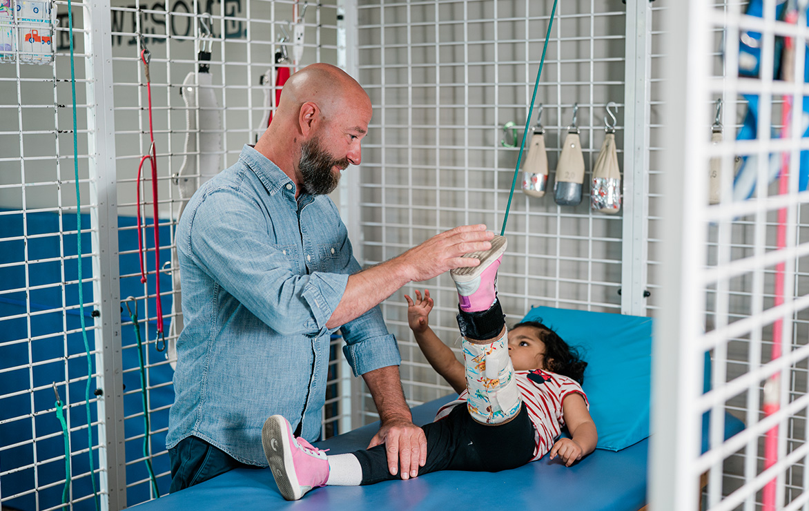 Adult assisting a child in a physical therapy session, lifting the child's leg.