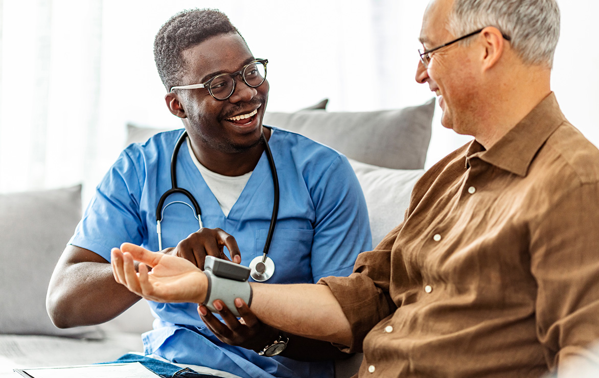A healthcare worker in blue scrubs taking a man's blood pressure.