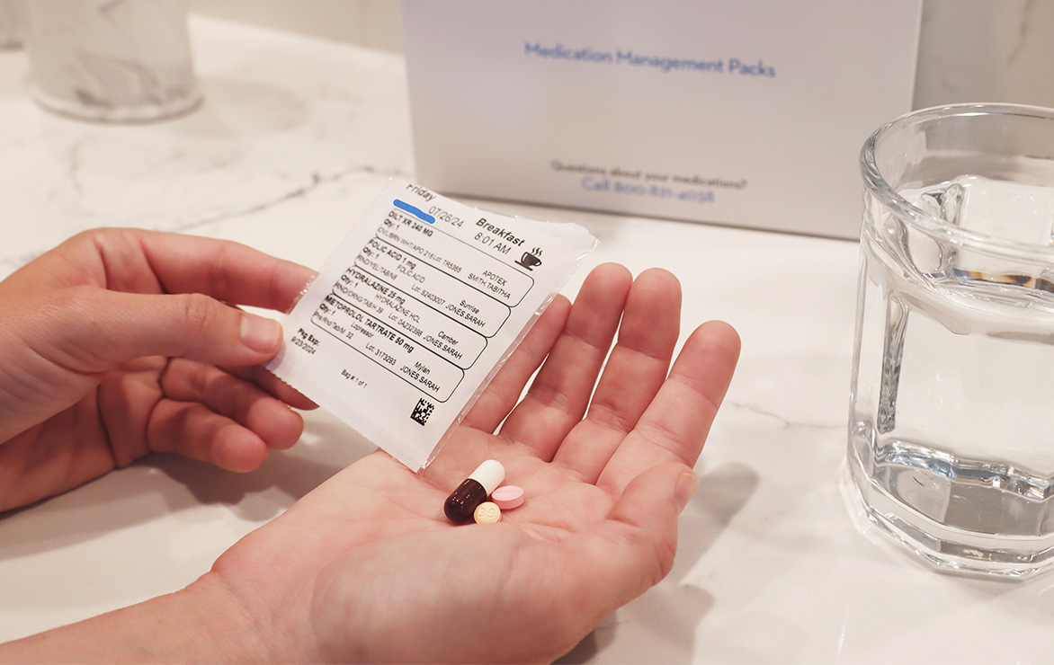 Hands holding a medication packet and pills, with a glass of water nearby.