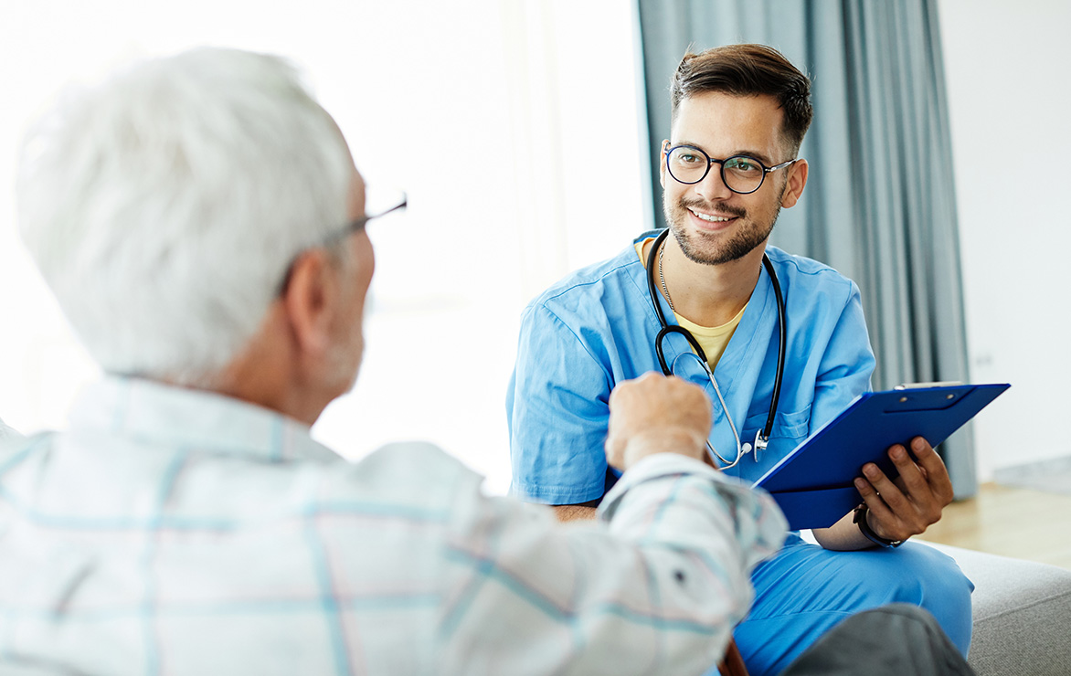 A healthcare professional smiling at an elderly man during a conversation.