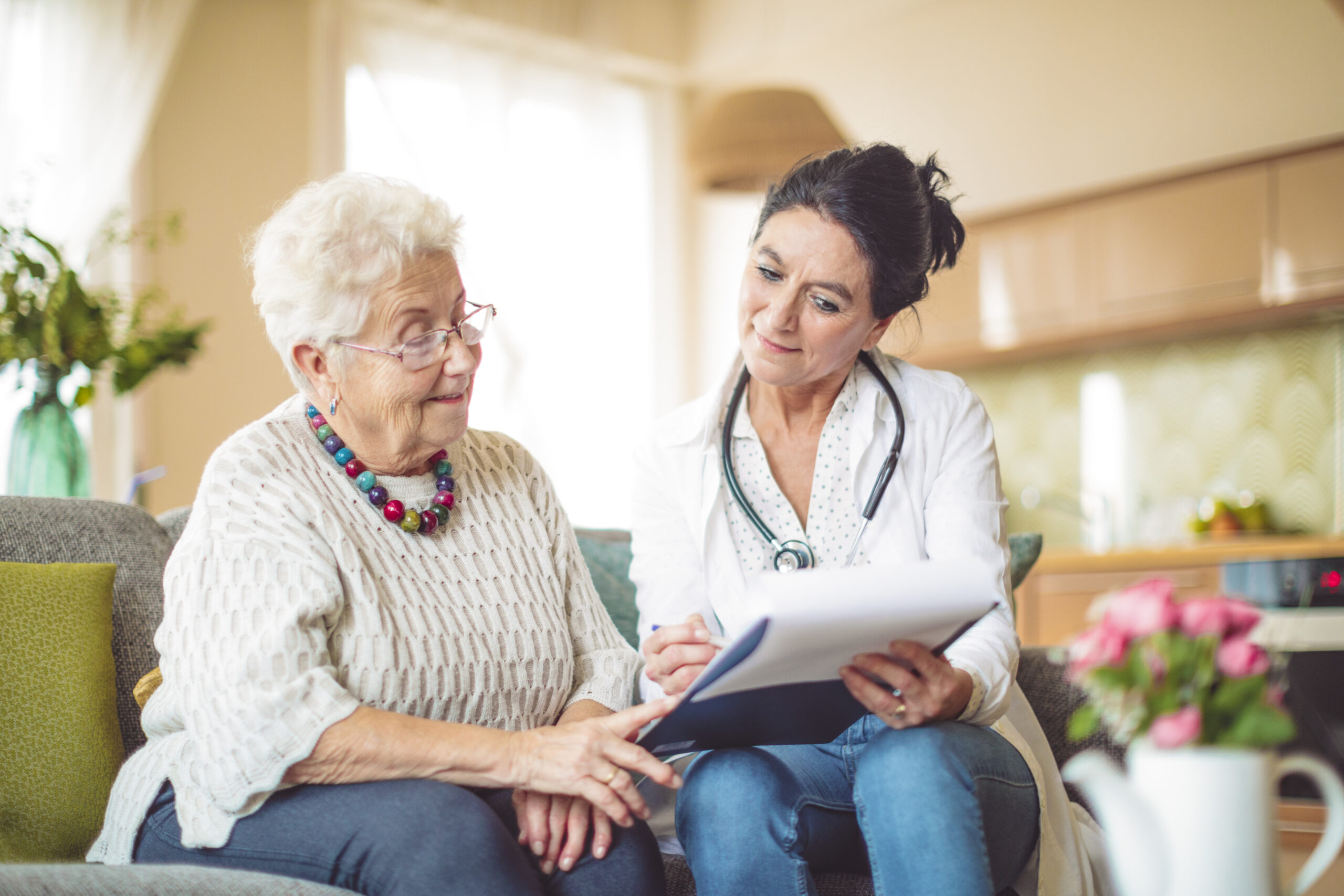 A doctor showing a medical report to her patient as they sit on the couch smiling and discussing the report.