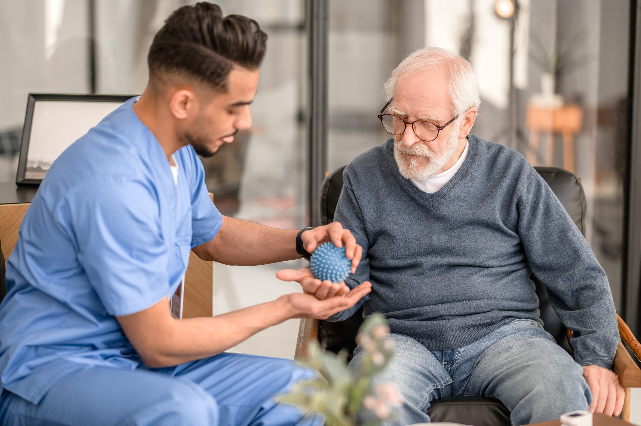 Focused rehabilitation physician massaging the palm of an elderly patient with a spiky massage ball