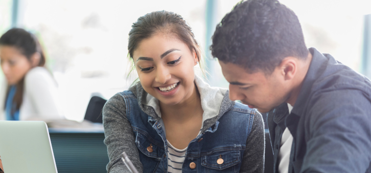 Two students collaborating and smiling over a notebook.