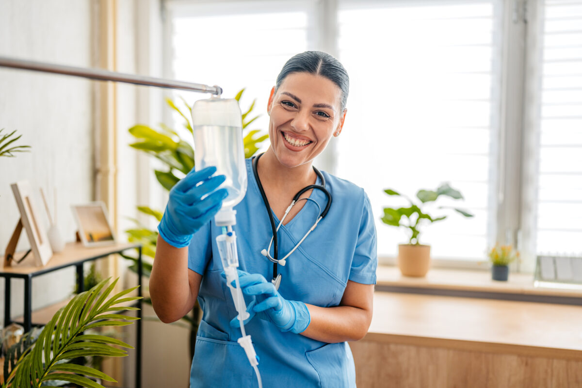 Female home care nurse adjusting and preparing an IV drip inside an apartment