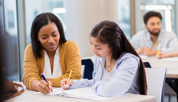 Two women studying together at a table, one guiding the other.