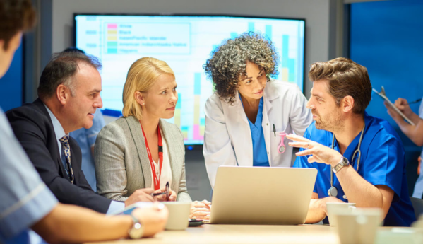 Medical professionals and business people in a discussion around a table with a laptop.