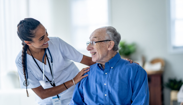 A healthcare worker smiles at an elderly man, while gently touching his shoulder.