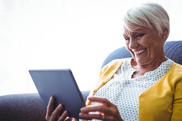 An older woman smiling while looking at a tablet computer